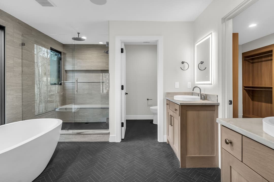 Modern bathroom with freestanding tub, glass shower, and dual vanities featuring wood cabinetry.