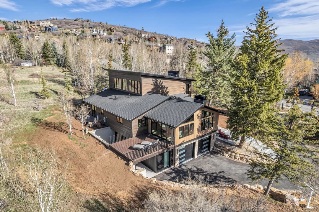 Modern mountain home featuring large windows and a spacious outdoor patio in a scenic landscape.