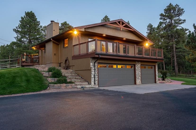 Modern two-story home with balcony, stone accents, and landscaped surroundings at dusk.