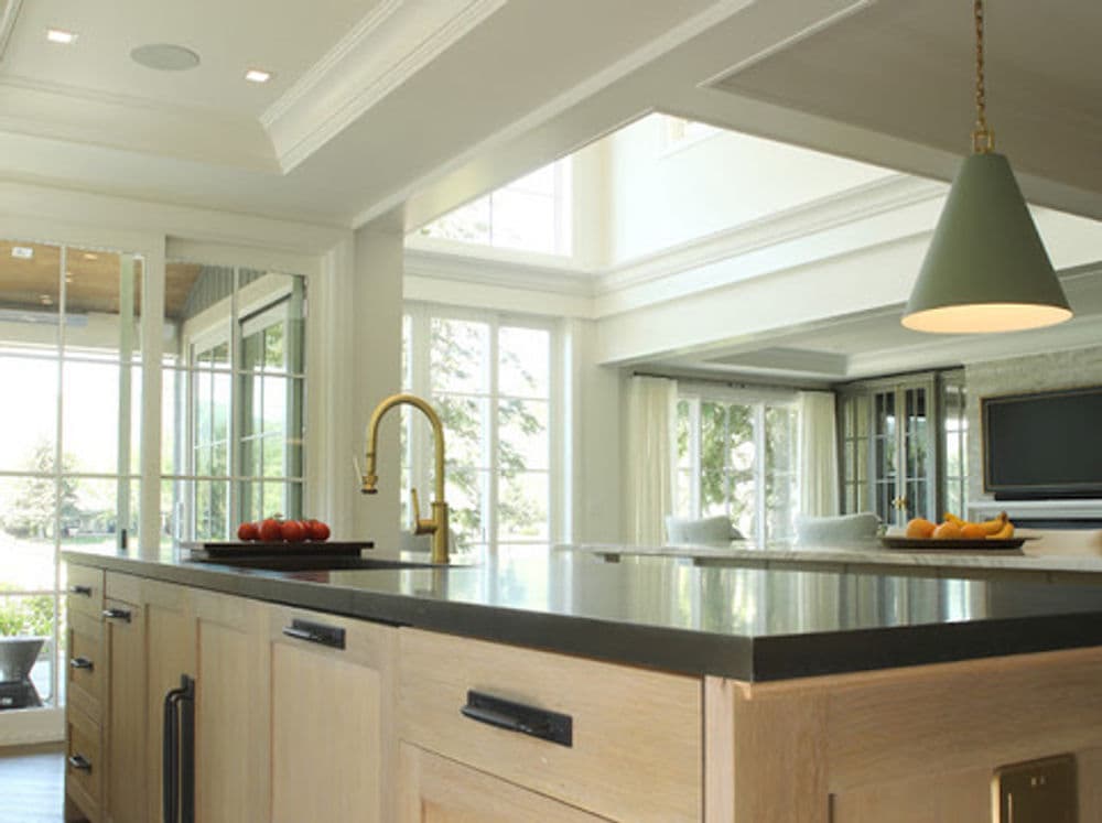 Modern kitchen with an island, gold faucet, green pendant light, and large windows.