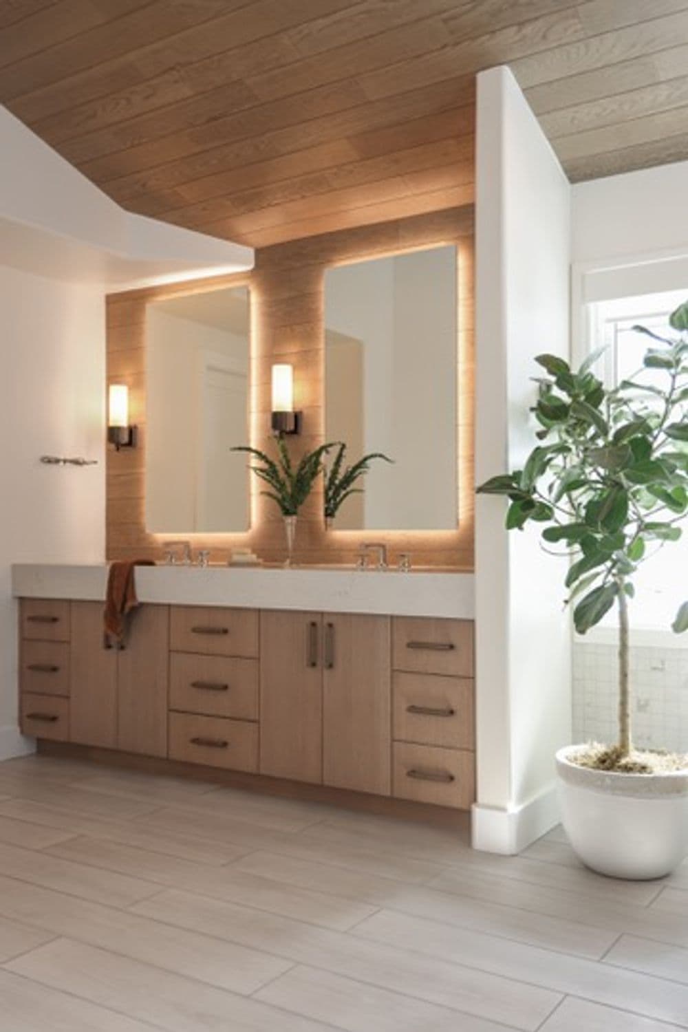 Modern bathroom with wood accents, double mirrors, sleek vanity, and green plant.