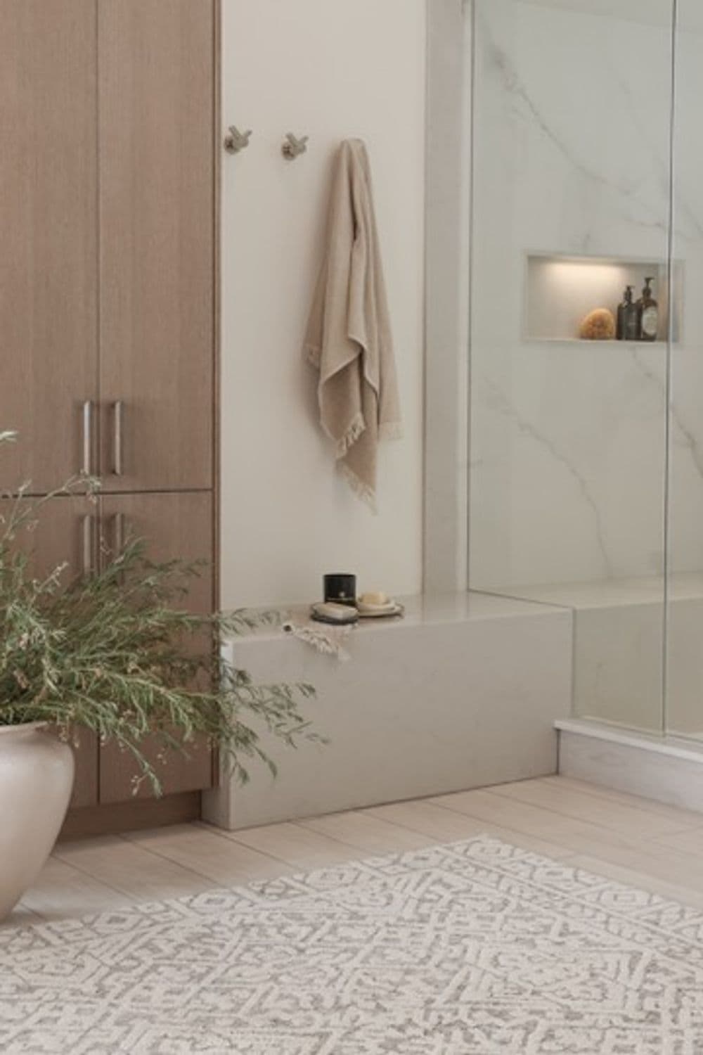 Modern bathroom interior with a marble bench, towel, and decorative plants on a patterned rug.