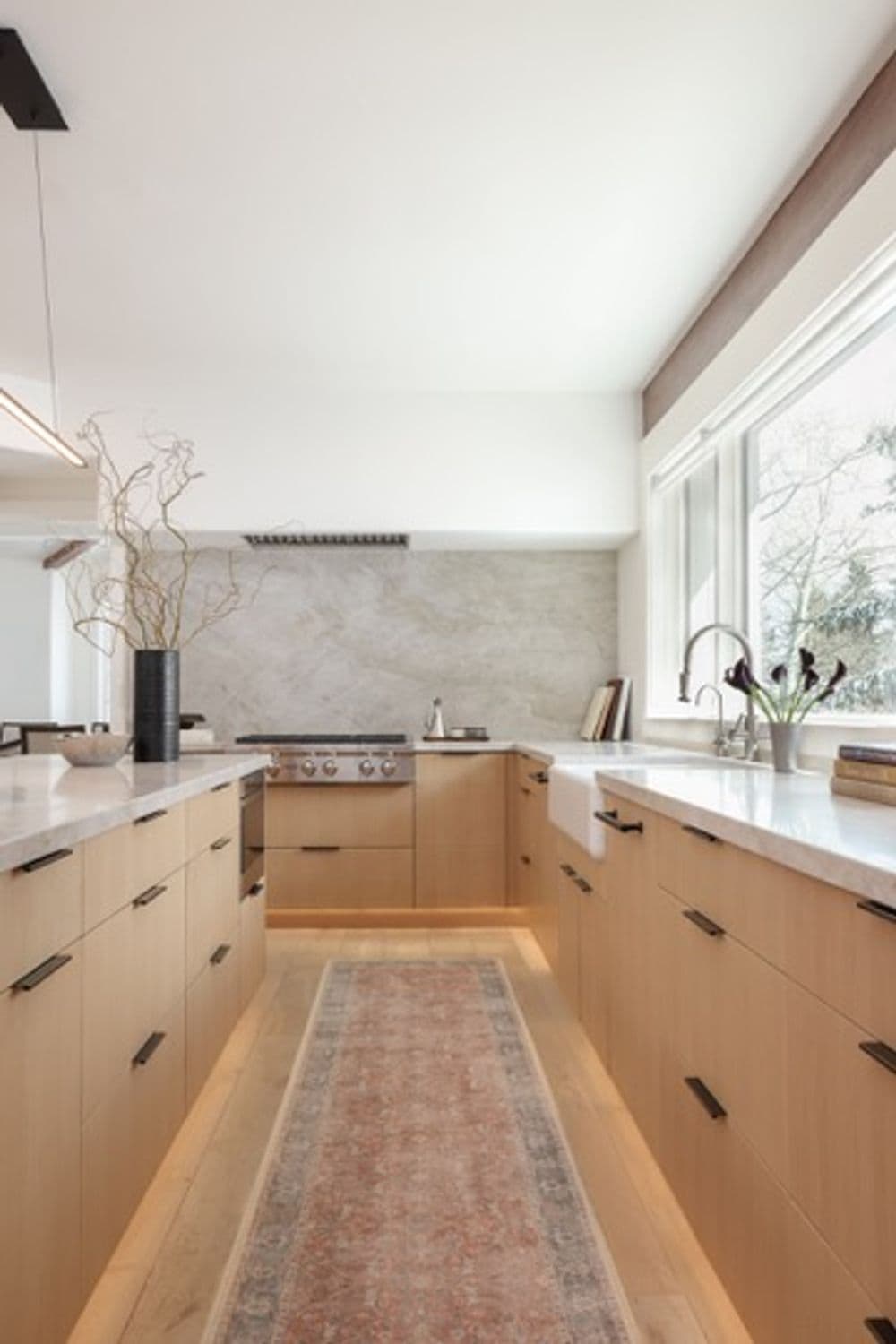 Modern kitchen with light wood cabinets, marble countertops, and a decorative area rug.