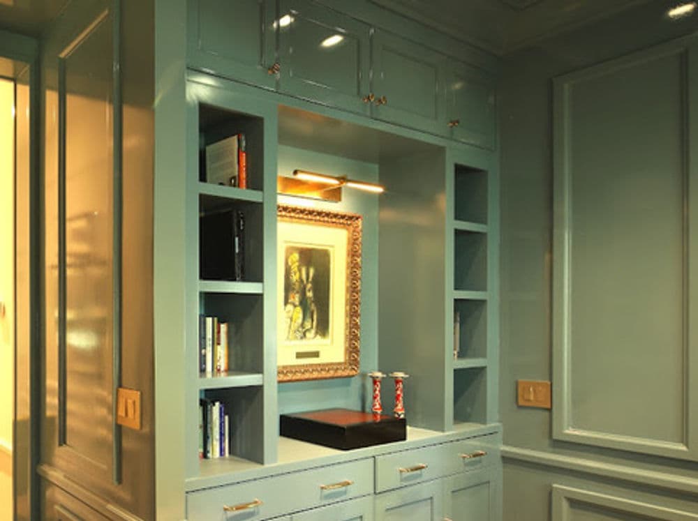 Elegant teal home office nook with bookshelves, framed art, and stylish lighting.