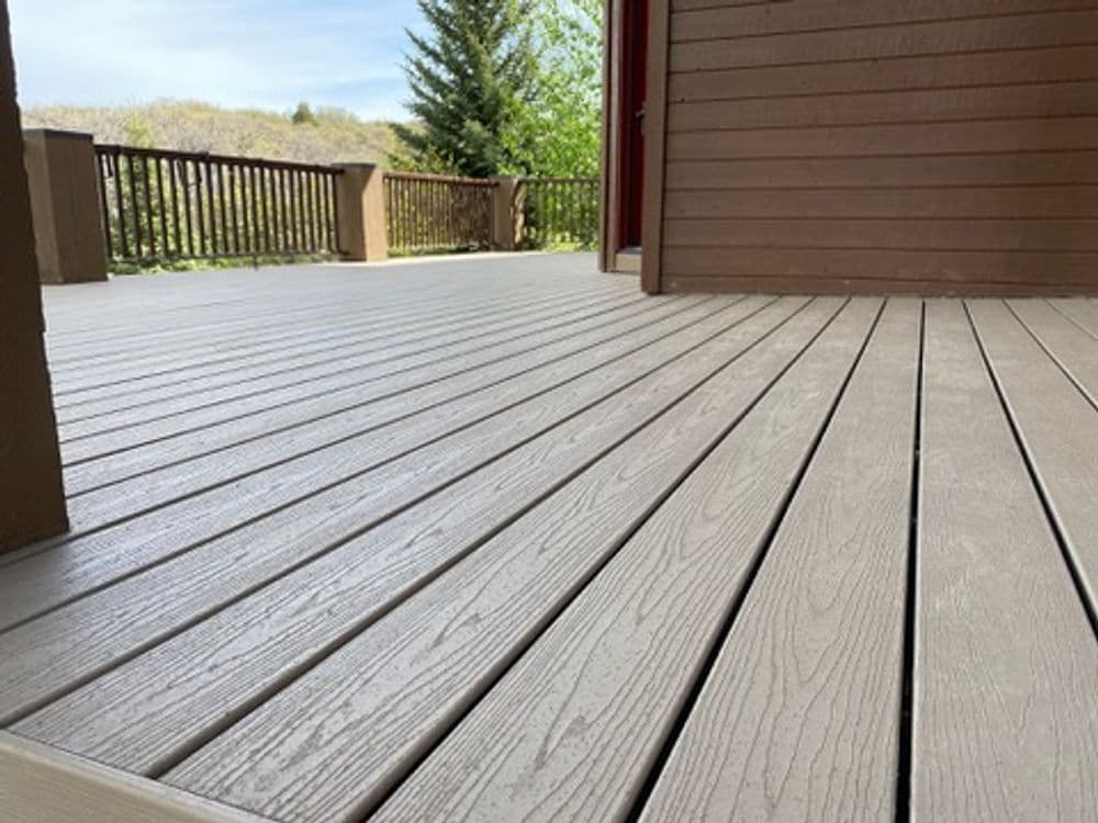 Composite decking on a spacious outdoor patio with wooden railings and green trees in the background.