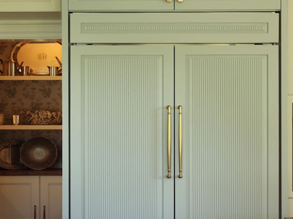 Modern mint green kitchen refrigerator with gold handles and detailed design.