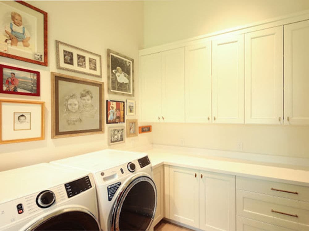Bright laundry room featuring modern washing machines, elegant cabinetry, and family photo gallery.