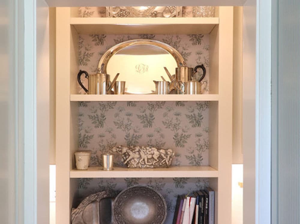 Decorative shelves with silverware, dishware, and books against a floral backdrop.