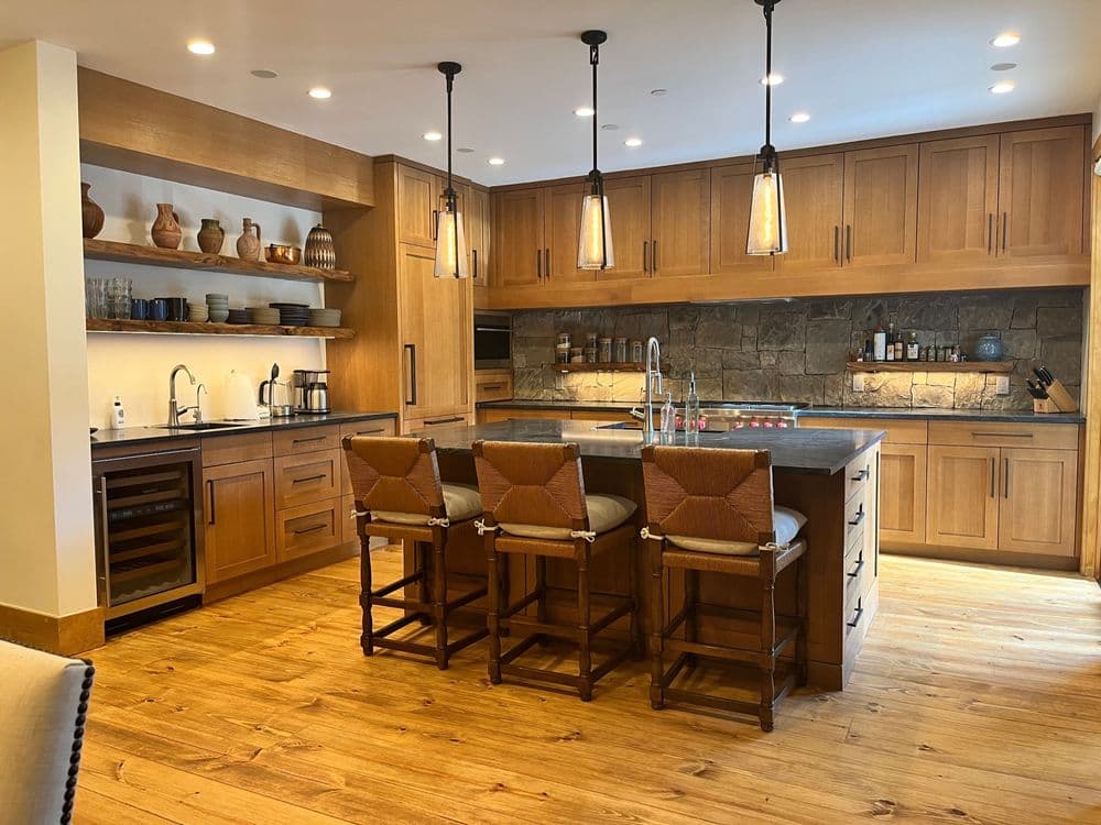 Modern kitchen with wooden cabinets, stone backsplash, island seating, and warm lighting.
