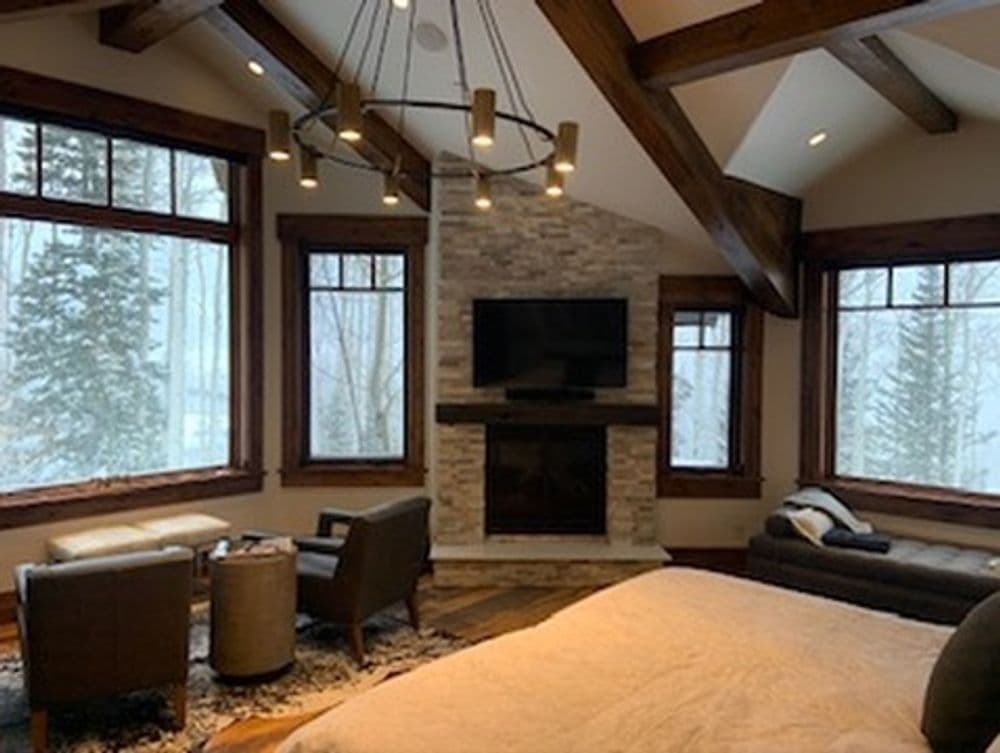 Cozy living room with large windows, stone fireplace, and modern decor surrounded by snow.