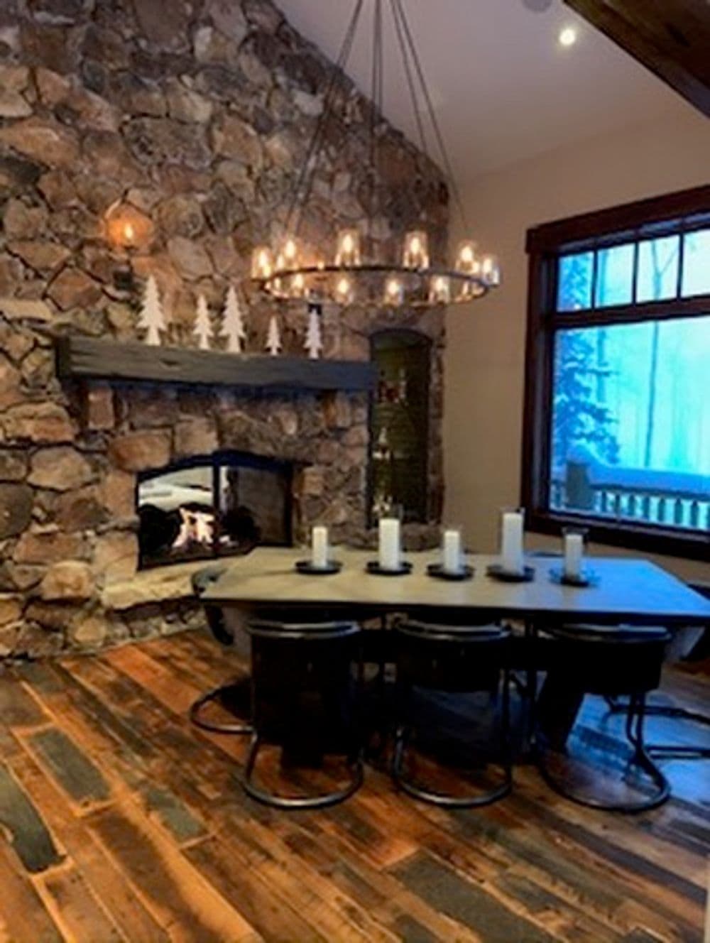 Rustic dining room with stone fireplace, wood accents, and large round table with candles.