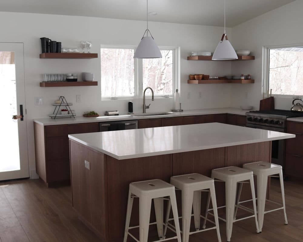 Modern kitchen with wooden cabinetry, white countertops, and stylish bar stools.