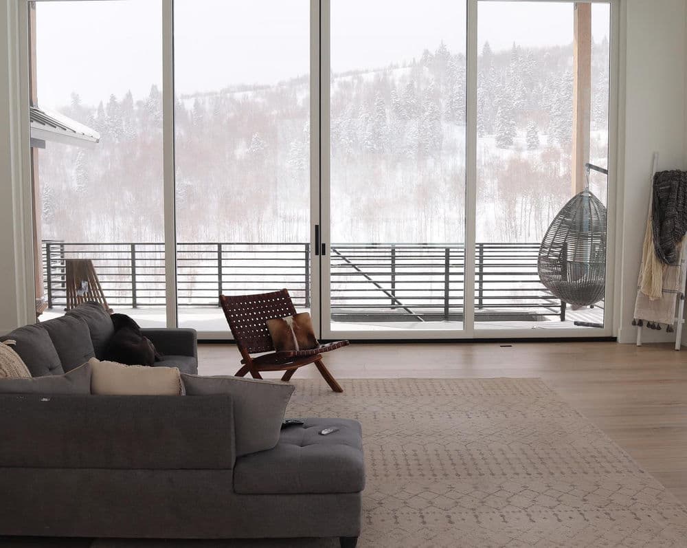 Modern living room with a cozy sofa, large windows, and a snowy mountain view outside.