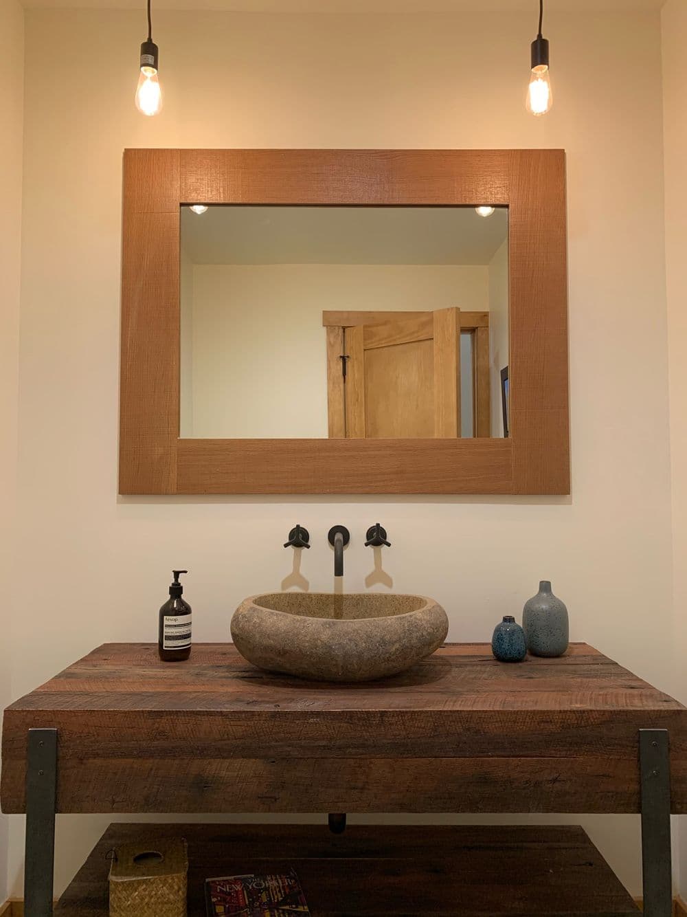 Stylish bathroom with stone sink, wooden mirror frame, and rustic decor on a wooden table.