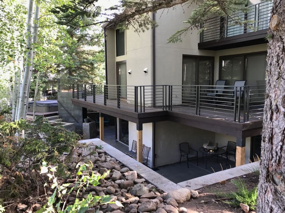 Modern two-story home with a balcony, surrounded by trees and landscaped rocks.