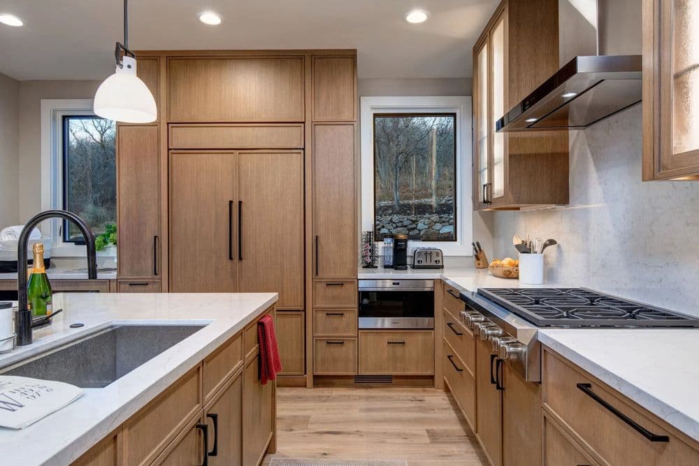 Modern kitchen with wooden cabinetry, stainless steel appliances, and marble countertops.