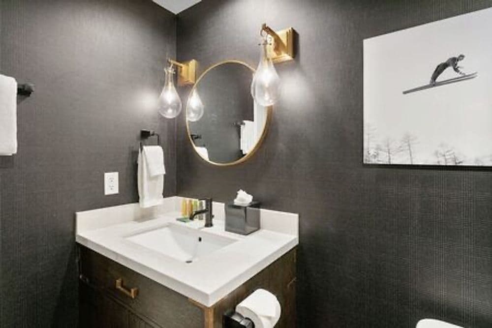 Modern bathroom with dark walls, round mirror, stylish light fixtures, and elegant sink.