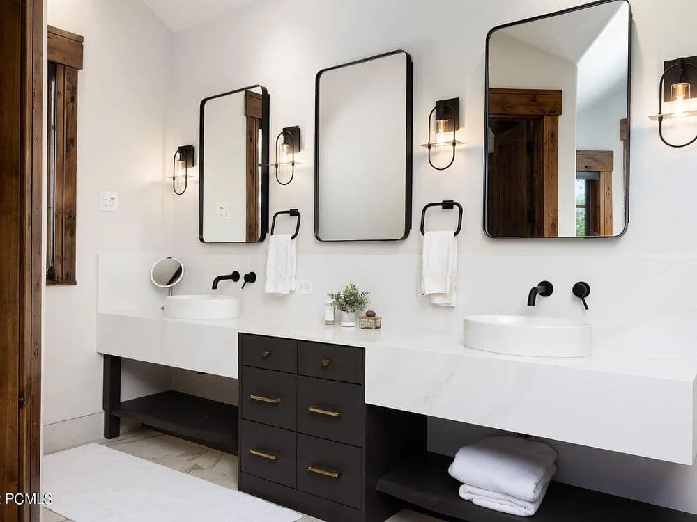 Modern bathroom with double sinks, black fixtures, and stylish mirrors on a white and wood backdrop.