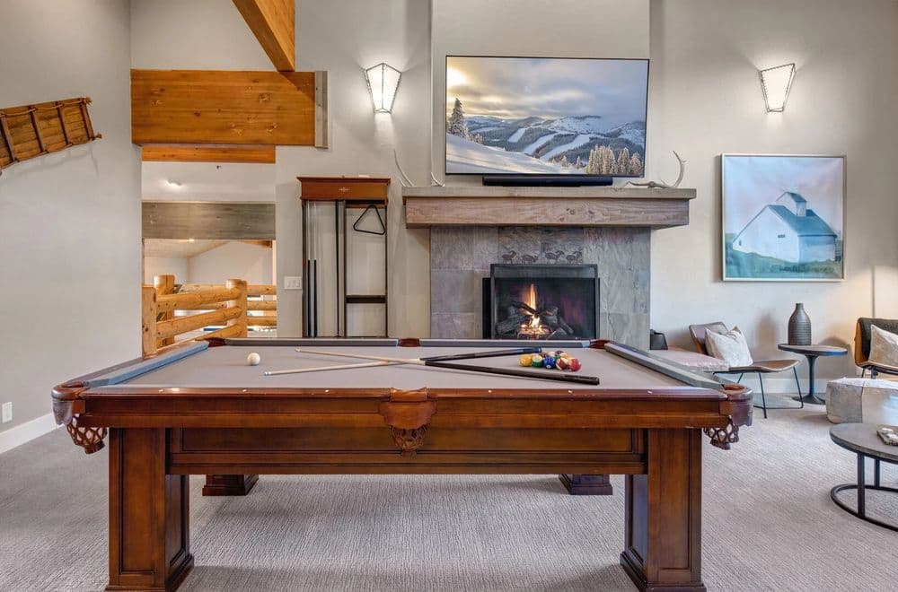 Modern living room with a pool table, fireplace, and large TV in a cozy cabin setting.