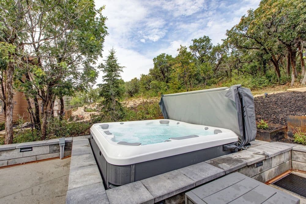 Outdoor hot tub with water, surrounded by lush trees and scenic landscape. Relaxation space.