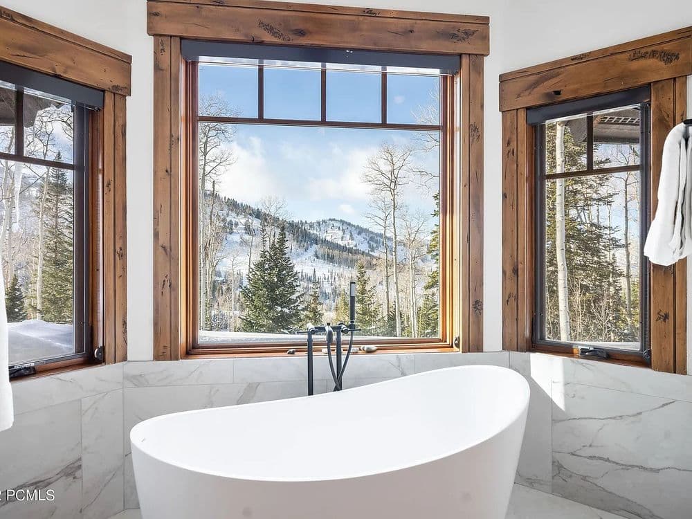 Luxurious bathroom with freestanding tub and stunning mountain views through large windows.